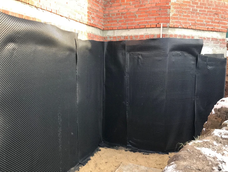 Chantier de construction extérieur montrant l'application d'un système d'étanchéité sur fondations