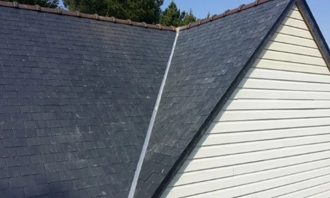 Maison traditionnelle anglaise avec toit de chaume épais et ondulant, murs en pierre calcaire beige, cheminée en brique avec antenne TV