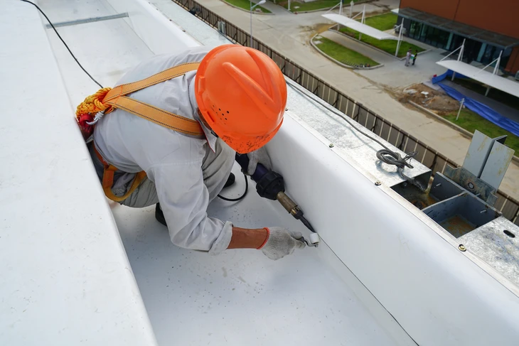 Ouvrier en hauteur effectuant des travaux d'étanchéité sur toiture-terrasse d'un bâtiment industriel