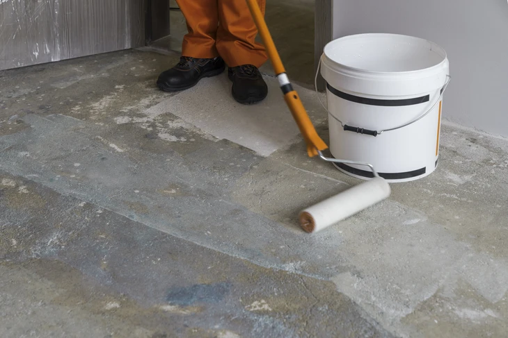 Ouvrier appliquant un revêtement sur sol béton avec rouleau à manche télescopique orange