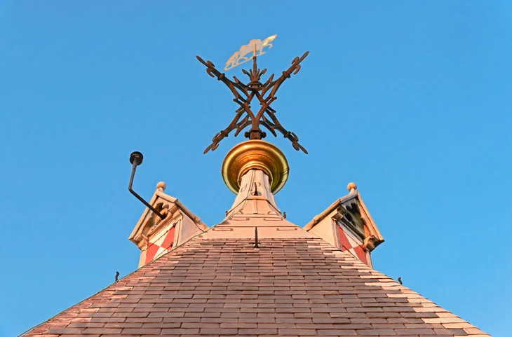 Extérieur, vue en contre-plongée d'une toiture pyramidale en ardoises avec charpente apparente et girouette décorative au sommet
