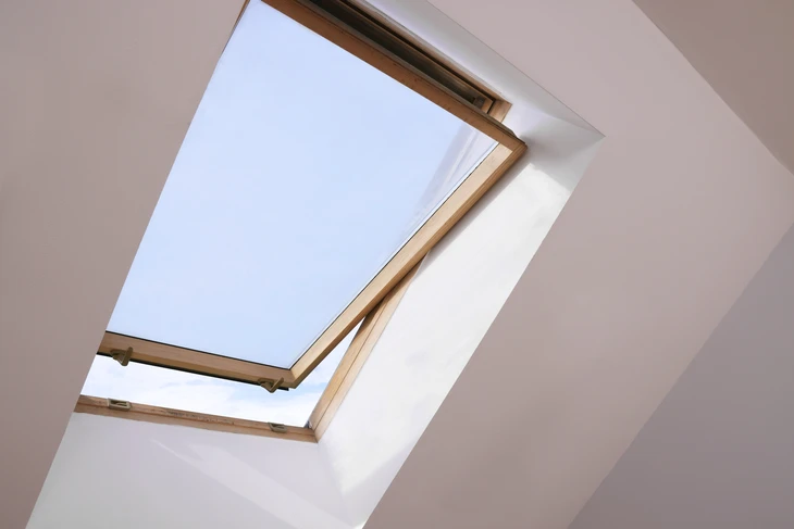 Fenêtre ouverte sur le toit de la lucarne sur plafond incliné dans la chambre mansardée