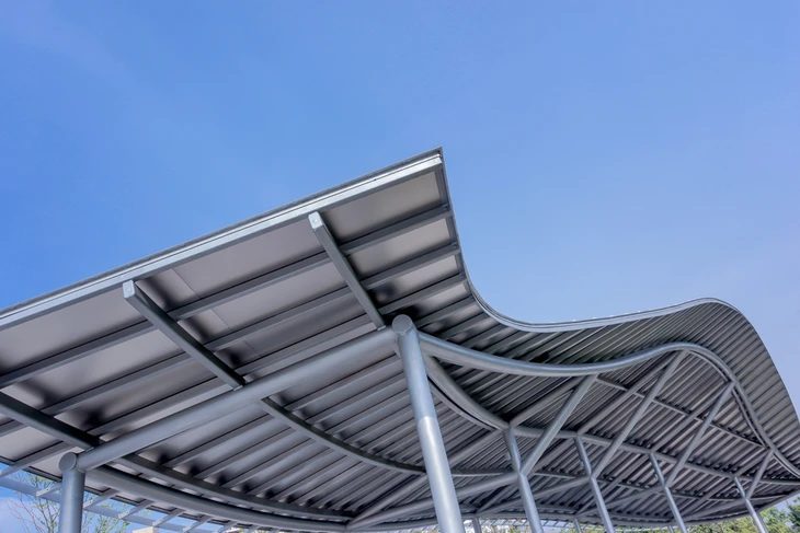 Structure métallique moderne avec toiture ondulée en tôle nervurée galvanisée, soutenue par charpente tubulaire acier peinte blanc