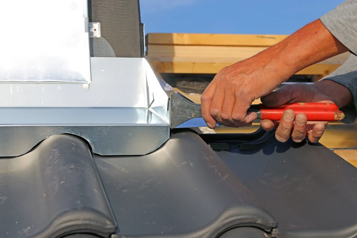 Chantier extérieur, ouvrier appliquant un produit d'étanchéité au niveau de la liaison entre tuiles et cheminée sur toiture