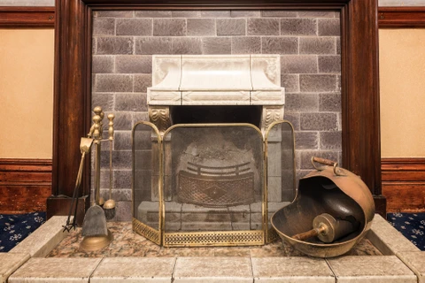 Cheminée traditionnelle en brique avec manteau décoratif sculpté, écran de protection en laiton à mailles fines, foyer avec grille métallique