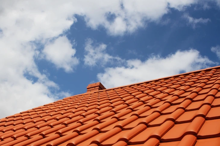 Toiture en tuiles de terre cuite rouge orangé vue en contre-plongée sous ciel bleu nuageux