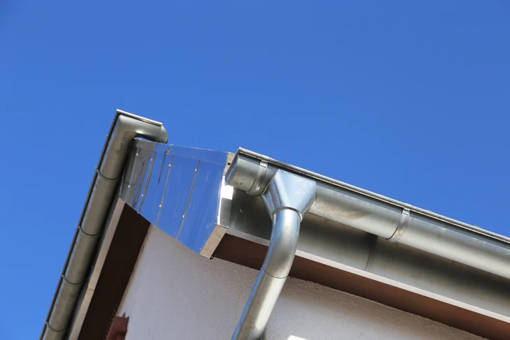 Extérieur d'un bâtiment moderne sous ciel bleu avec système d'évacuation des eaux pluviales visible en partie haute de la façade