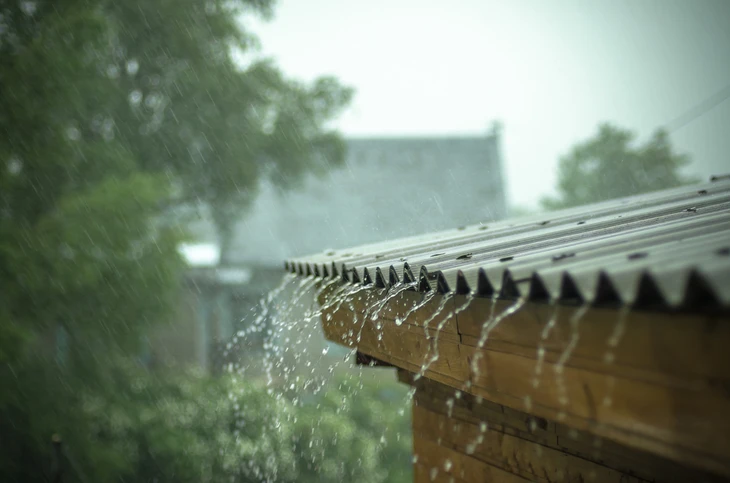 Extérieur sous forte pluie, gouttière métallique débordante évacuant l'eau de toiture par ruissellement
