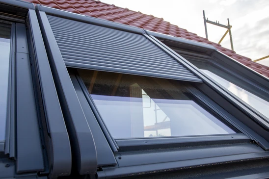 Intérieur moderne d'un comble ou grenier mansardé, baigné de lumière naturelle diffusée par une fenêtre de toit de style VELUX. La pièce montre un espace de vie confortable avec murs clairs, mobilier élégant, et la lumière naturelle créant une ambiance chaleureuse et accueillante. Vue depuis l'intérieur, mettant l'accent sur le confort lumineux apporté par la fenêtre.