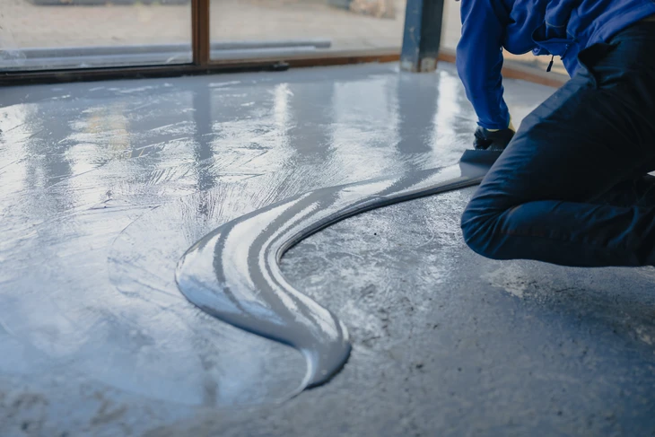 Ouvrier en combinaison bleue appliquant un revêtement de sol liquide à l'intérieur d'un bâtiment