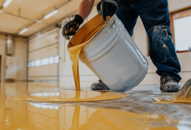 Ouvrier appliquant un revêtement de sol liquide jaune dans un atelier industriel