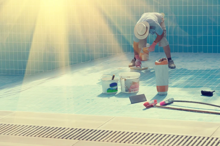 Ouvrier en combinaison et chapeau appliquant un revêtement étanche dans une piscine vide carrelée