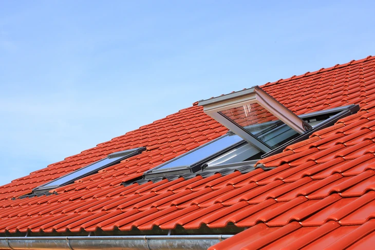 Extérieur d'une habitation avec toiture en tuiles terre cuite rouge sous ciel bleu dégagé