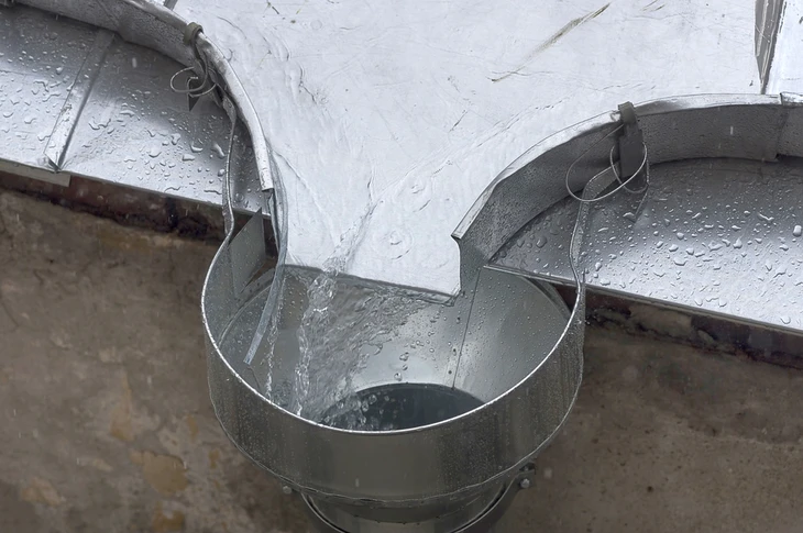 Extérieur, installation de récupération d'eau pluviale avec gouttière métallique déversant dans récipient cylindrique