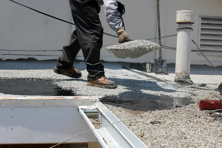 Ouvrier en tenue de travail appliquant un revêtement d'étanchéité sur toiture-terrasse