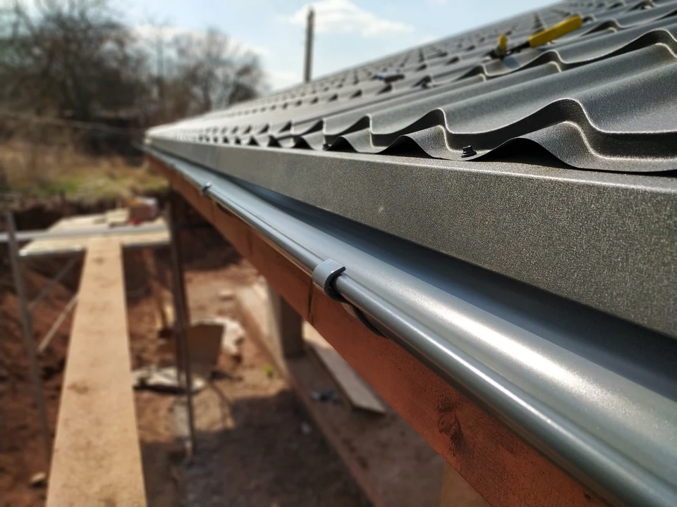 Chantier de construction résidentielle en extérieur, toiture en tuiles métalliques grises ondulées avec gouttière aluminium installée