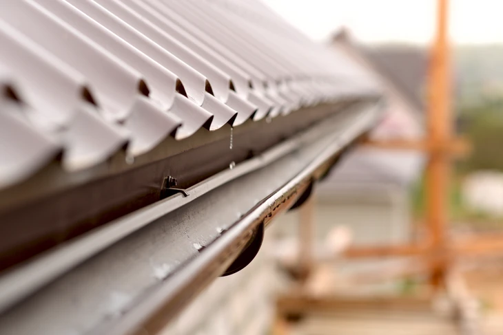 Gros plan sur une gouttière en aluminium avec système de protection anti-feuilles installé sur le rebord d'un toit résidentiel