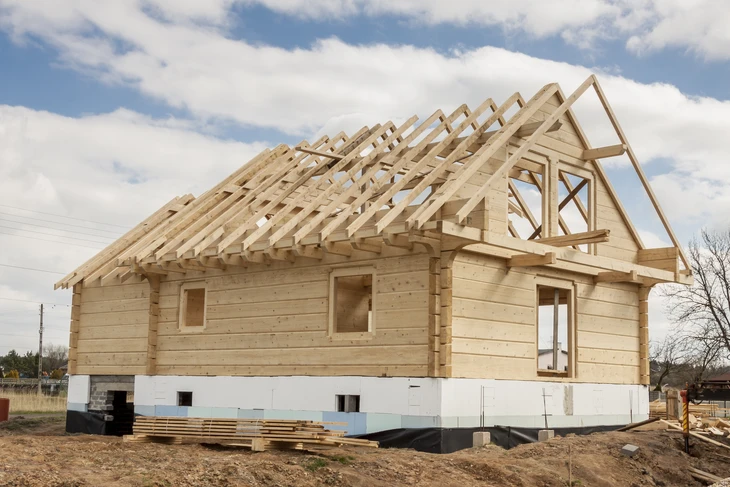 Chantier de construction d'une maison individuelle avec charpente bois apparente et murs en rondins