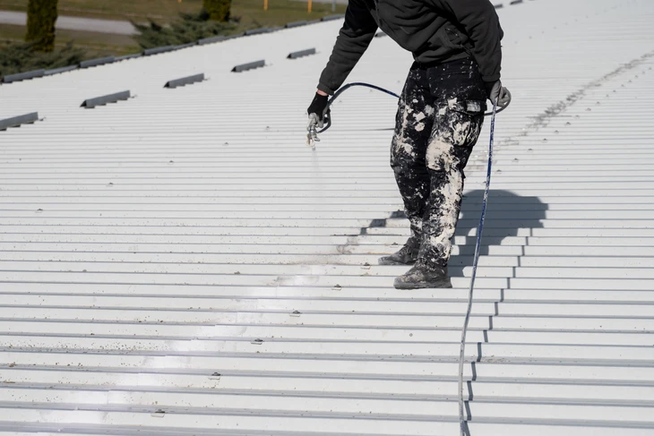 Ouvrier en équipement de protection appliquant un revêtement d'étanchéité sur toiture métallique industrielle