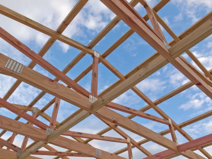 Chantier de construction extérieur avec charpente en bois en cours d'assemblage sous ciel bleu nuageux