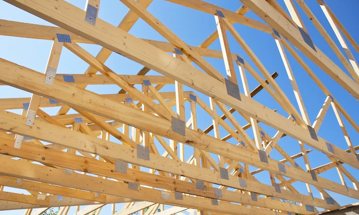 Chantier de construction extérieur avec charpente en bois en cours d'assemblage sous ciel bleu