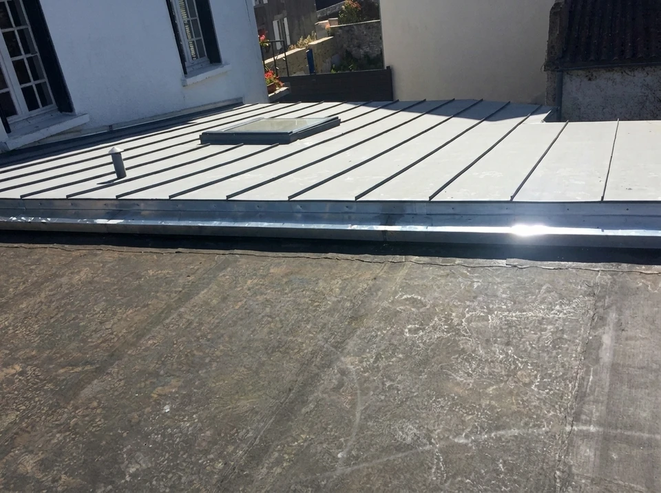 Un couvreur expérimenté effectuant des travaux de couverture sur un toit résidentiel en journée, manipulant des matériaux de toiture de qualité (ardoise ou tuiles), en tenue professionnelle de chantier. La scène montre le professionnalisme et le savoir-faire artisanal, mettant en avant la maîtrise technique d'un métier transmis depuis des générations. L'arrière-plan doit montrer une habitation résidentielle typique de Loire-Atlantique, en bon état, illustrant un travail de qualité réalisé avec expertise.