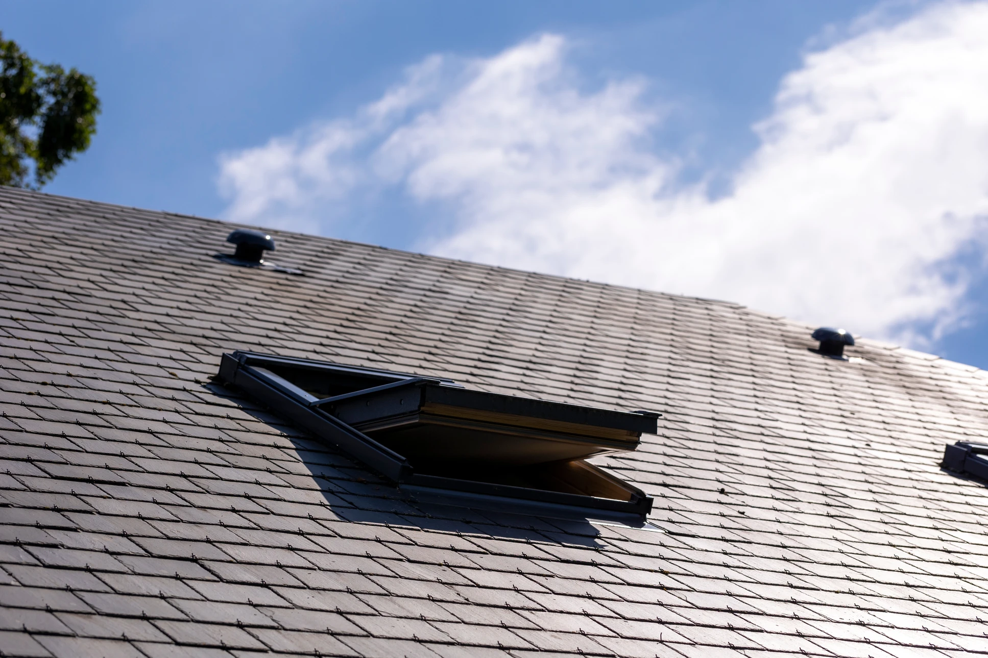 Photographie en plongée d'un comble ensoleillé avec une fenêtre de toit nouvellement posée (type Velux), laissant entrer la lumière naturelle sur les poutres apparentes ou l'aménagement intérieur du comble. La fenêtre doit être clairement visible comme un élément de couverture/zinguerie professionnelle, avec une lumière douce et abondante mettant en avant la transformation de l'espace.